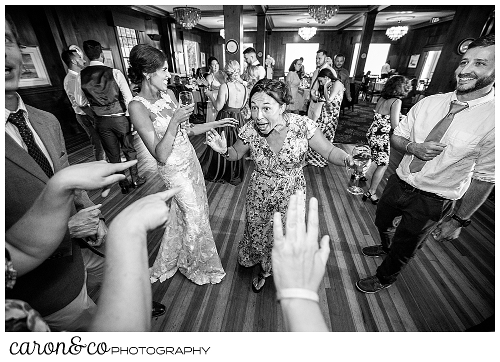 a black and white photo of a bride dancing with a friend, hands in the foreground are pointing to the women