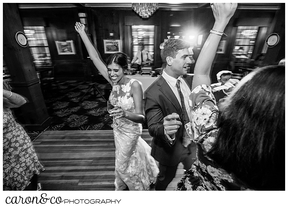 a bride on the dance floor with wedding guests, her arm is raised above her head