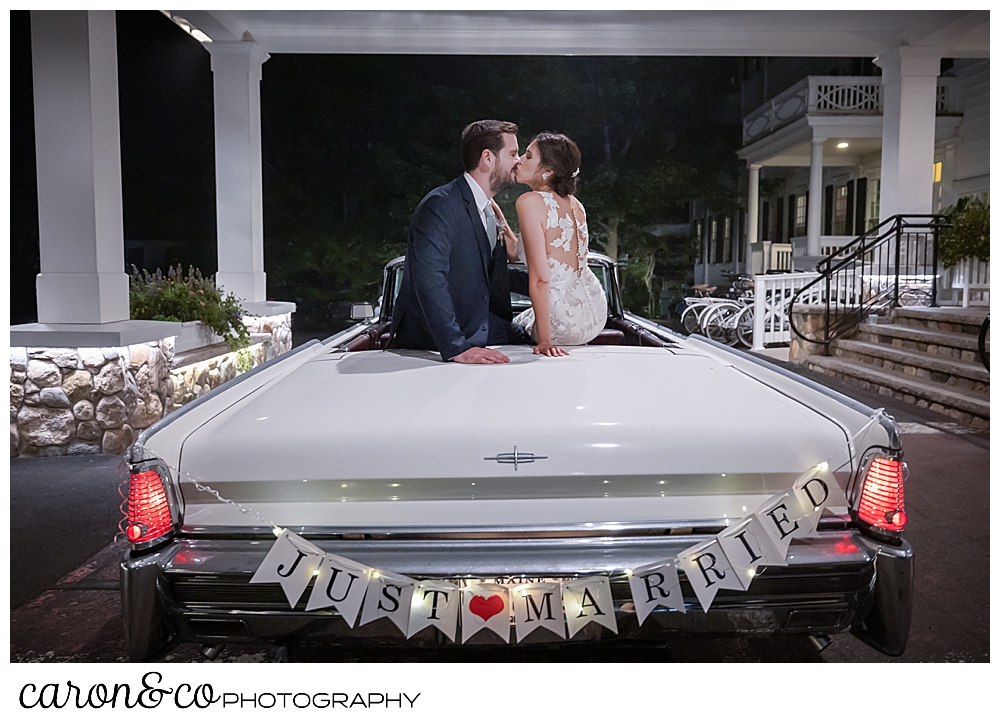 a bride and groom sitting on the back of a vintage white Lincoln Continental convertible with the top down, they are kissing, and the sign on the bumper reads just married, at the steps of the Colony Hotel Kennebunkport Maine