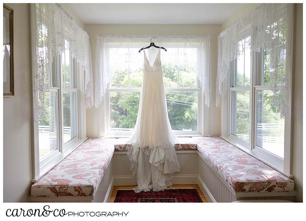 a wedding dress hangs in a alcove of windows