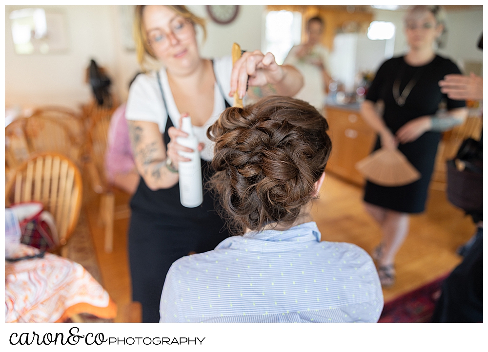 a bride having an updo done, gets sprayed with hairspray