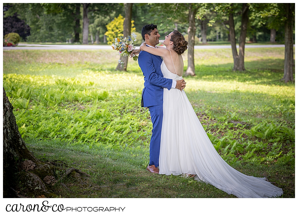 a bride in a sleeveless white dress hugs her groom who is wearing a blue suit, during their Maine wedding day first look