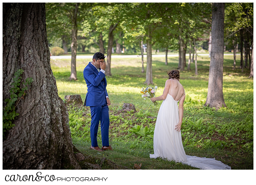 a groom dressed in blue, puts his hand to his eyes, as he views his bride to be during their Maine wedding day first look