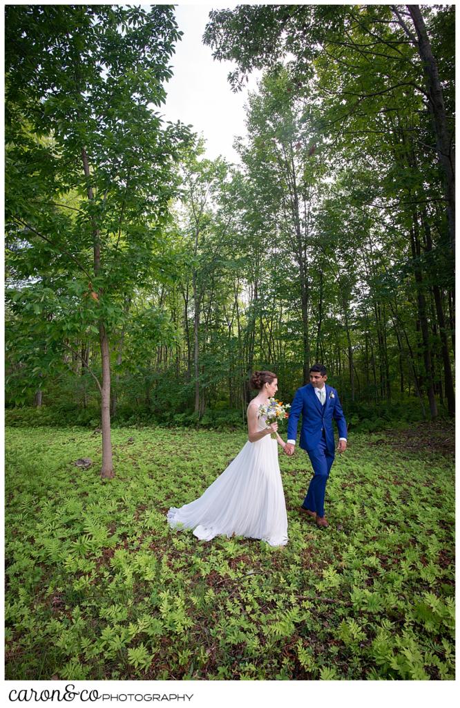 a bride and groom walk together through the woods