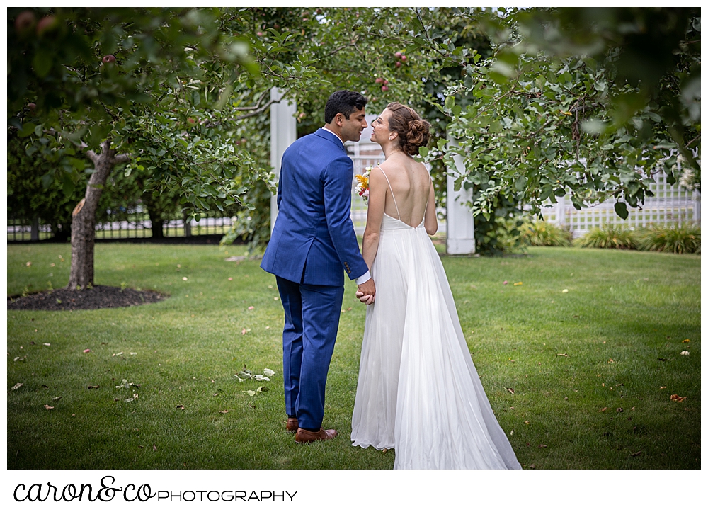 a bride and groom, their backs to the camera, are about to kiss as they walk away