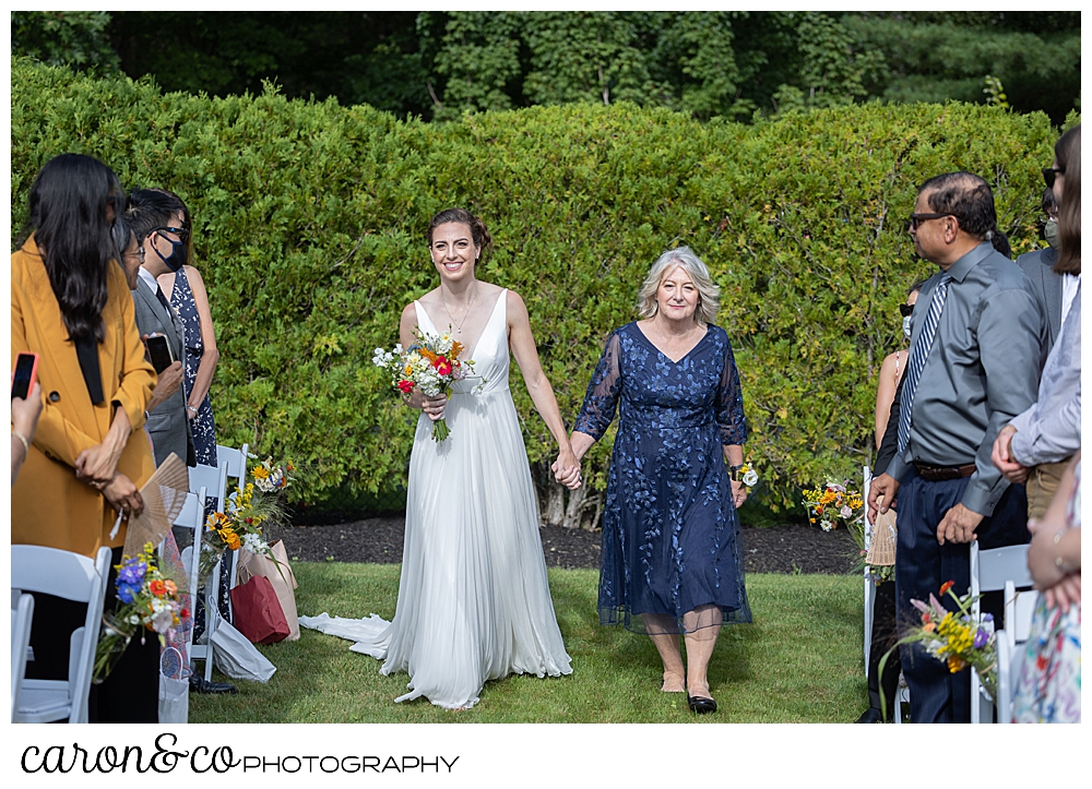 a bride and her mother walk down the aisle at a joyful Pineland Farms wedding in the Garden