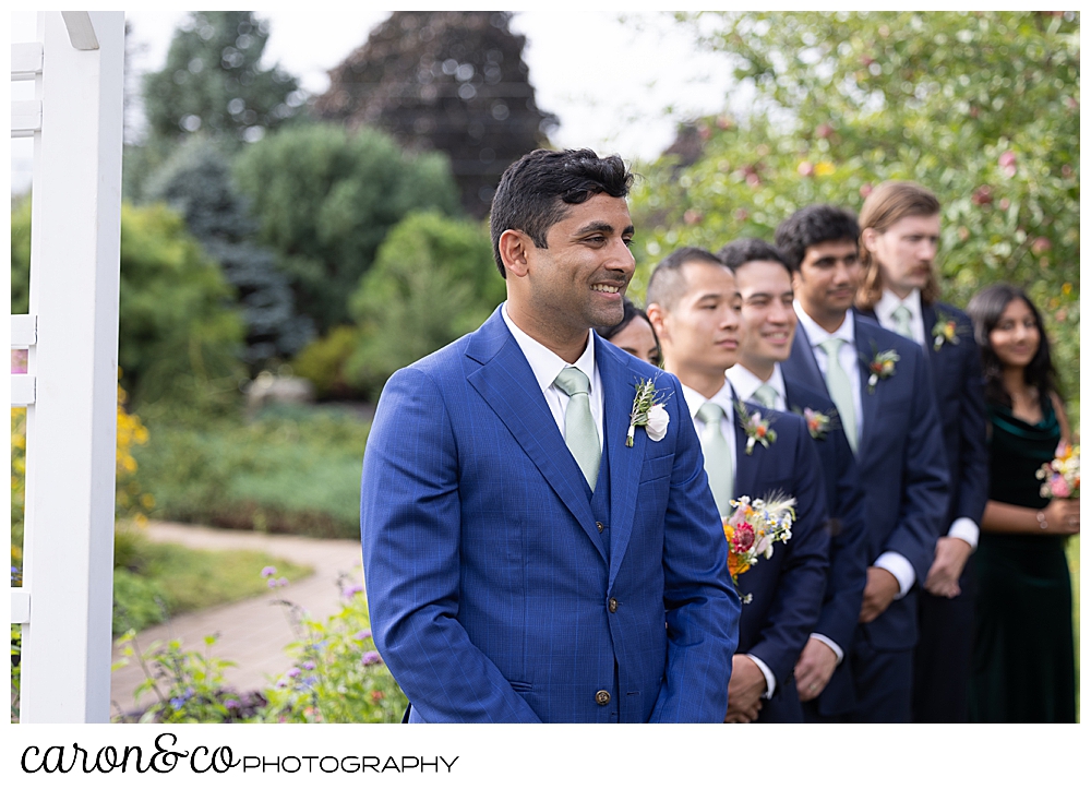 a groom smiles as he waits for the bride to walk down the aisle at a Pineland Farms garden ceremony