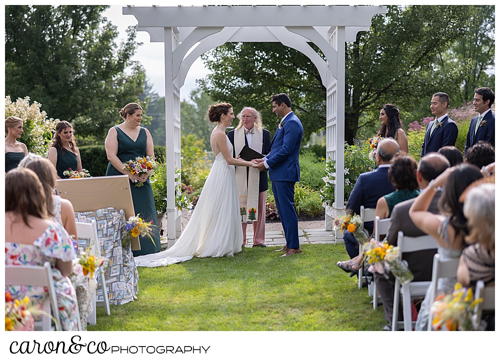 a bride and groom stand under a pergola at a joyful Pineland Farms wedding ceremonh