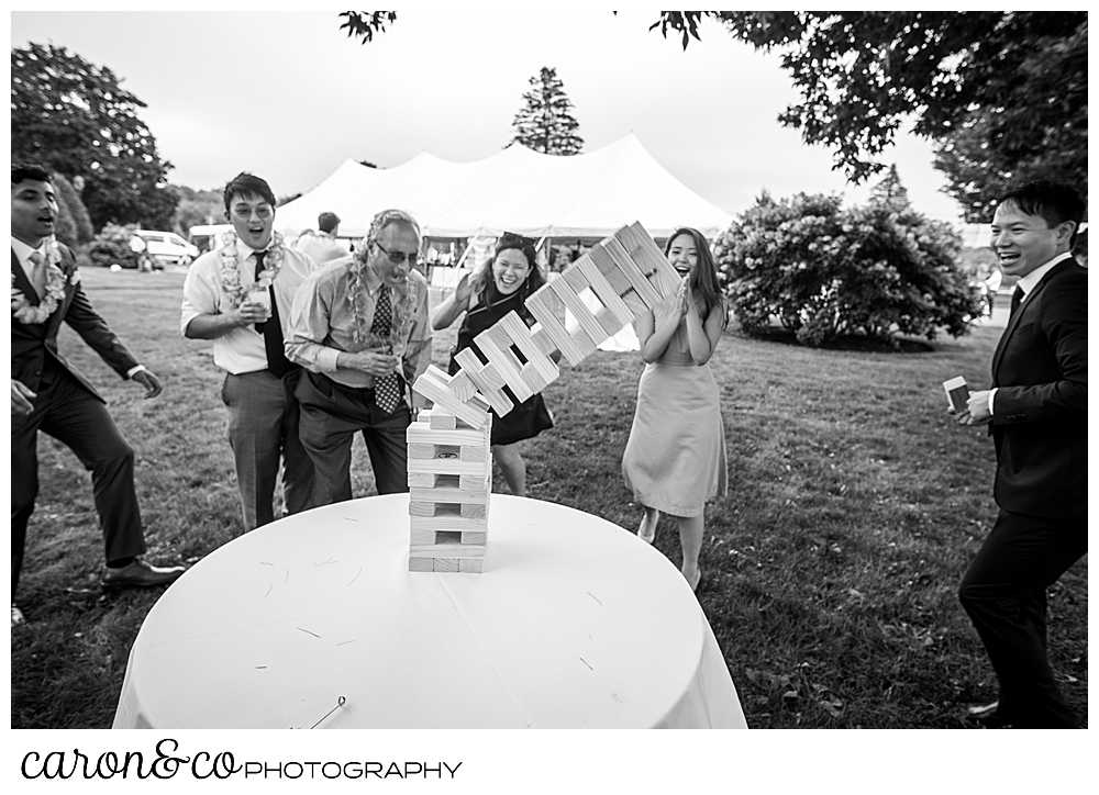 black and white photo of wedding guests playing Jenga, and the tower is falling over