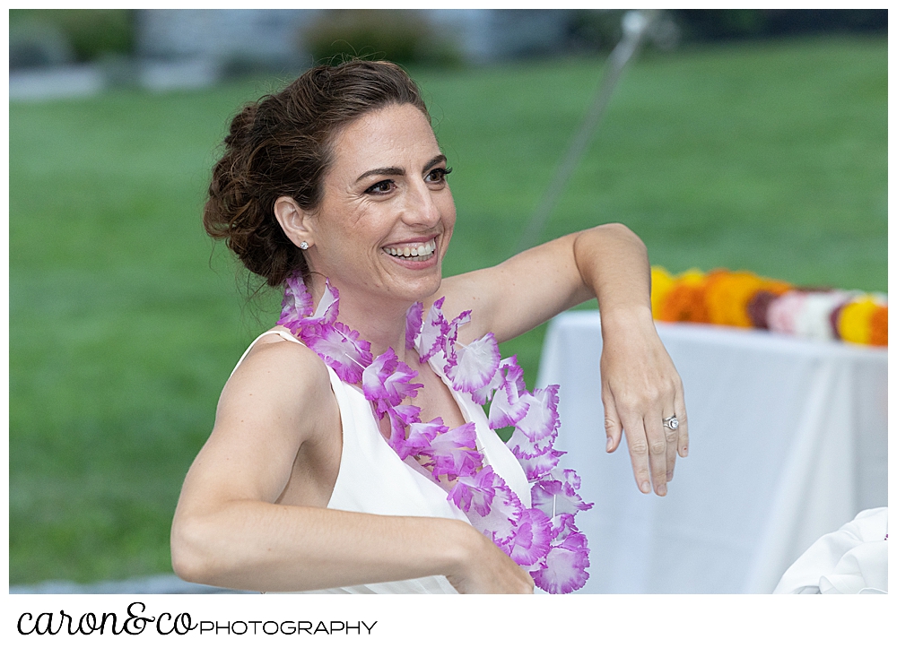 a bride leans her arm on her chair, and smiles at a joyful Pineland Farms wedding reception