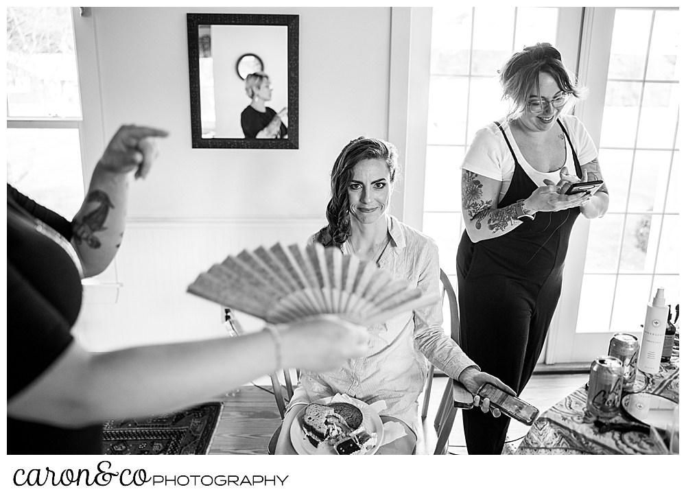 black and white photo of a bride having her hair done, gets fanned while trying to cool off