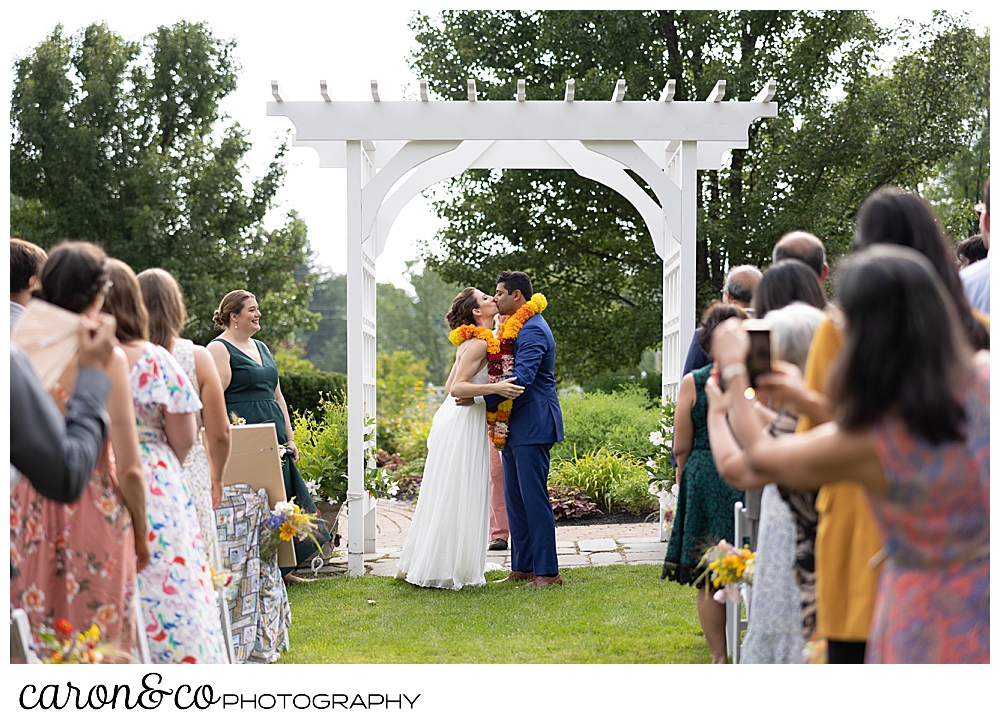 a bride and groom share their first kiss under a pergola at their joyful Pineland farms wedding ceremony