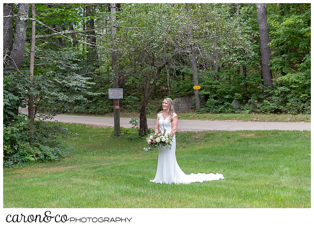 a bride is standing in a grassy field, wearing a white dress, carrying a bridal bouquet, during her Kingsley pines maine wedding day first look