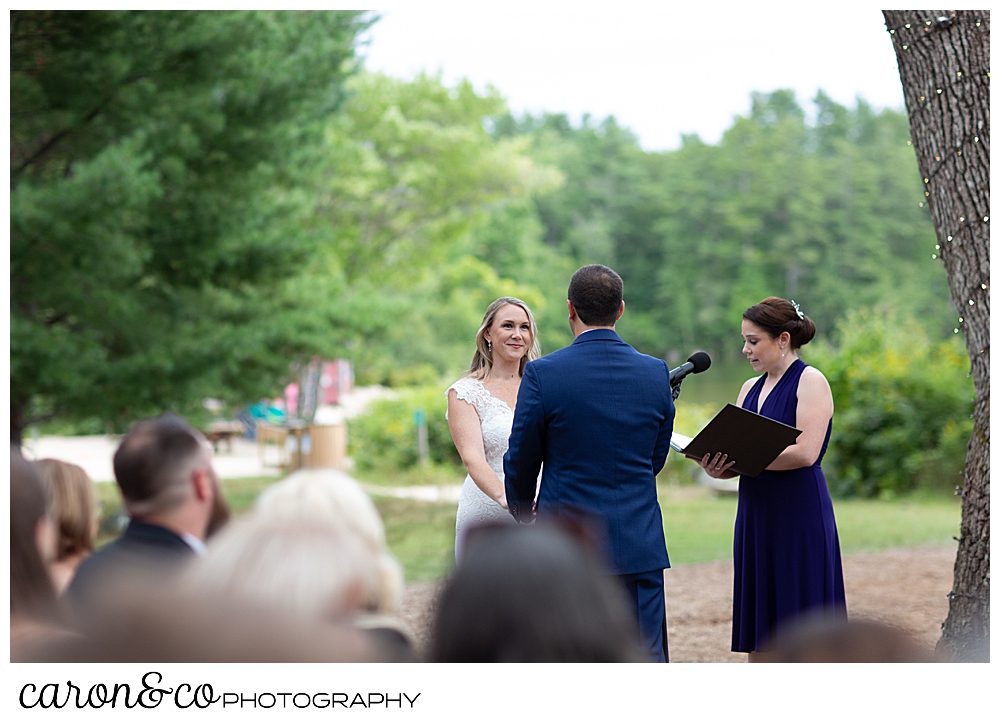 a bride and groom stand together in front of their officiant at a Kingsley Pines Maine wedding ceremony