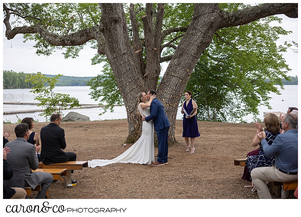 a bride and groom have their first kiss at the ceremony tree at a Kingsley Pines Maine wedding ceremony