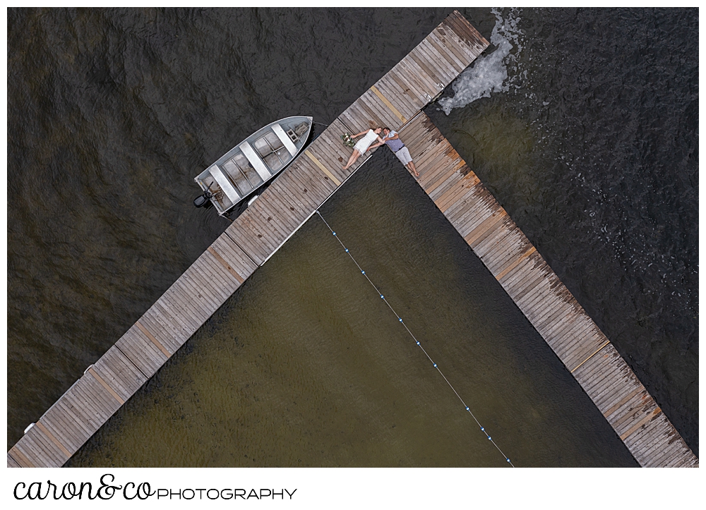 a drone photo of a bride and groom laying on the corners of a dock at Kingsley Pines, Raymond, Maine