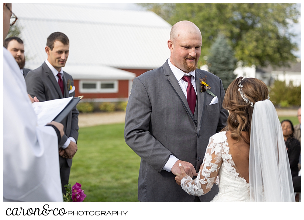 a groom holds his brides hands, and smiles during their wedding at Maine wedding barn in Minot Maine