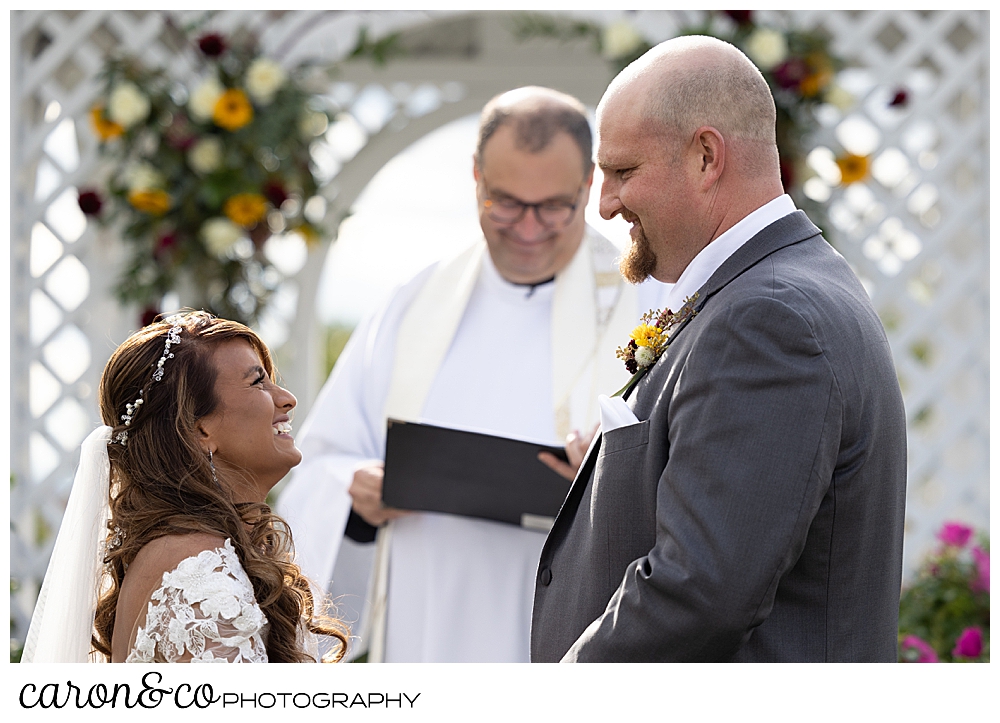 a bride and groom standing before their officiant, smile at one another
