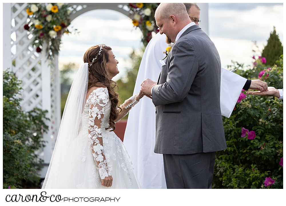 a bride and groom stand facing each other as the groom puts the bride's wedding band on her finger