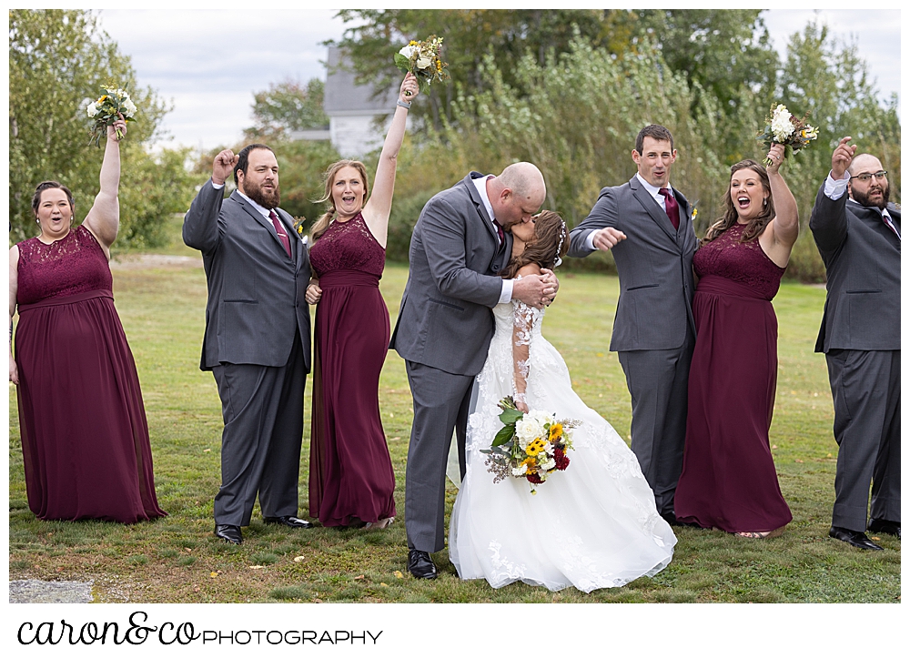 a bride and groom kiss while their bridal party cheers