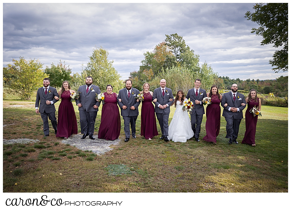 a bridal party with linked arms, walks toward the photographers