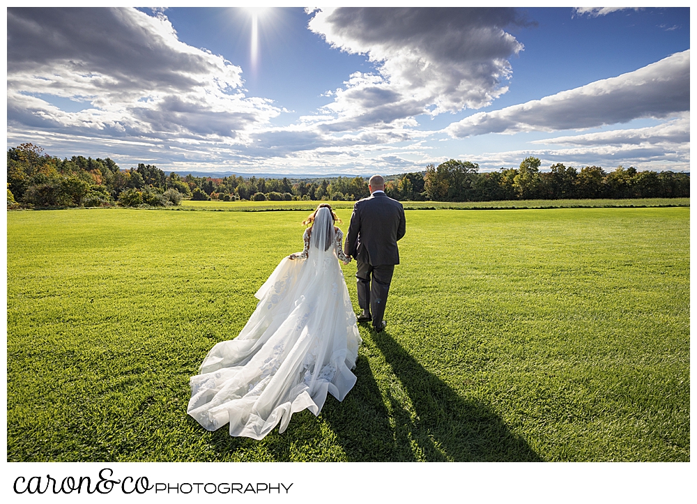 a bride and groom walk away in a grassy field at a wedding at Maine wedding barn in Minot Maine