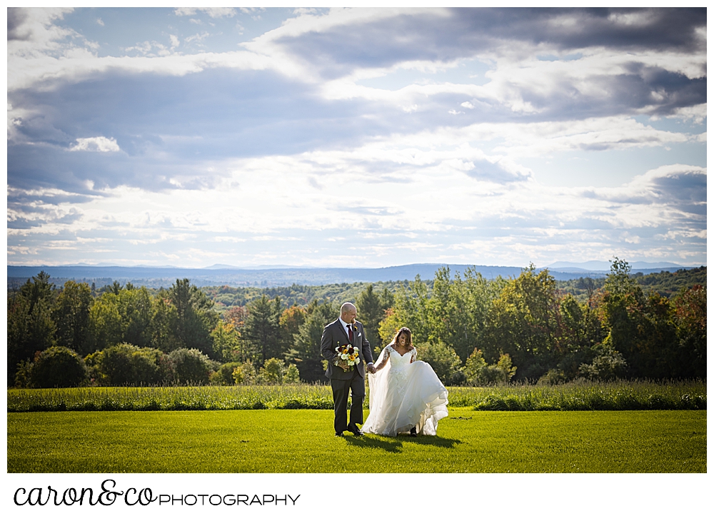 a bride and groom walk across a grassy field toward the photographer