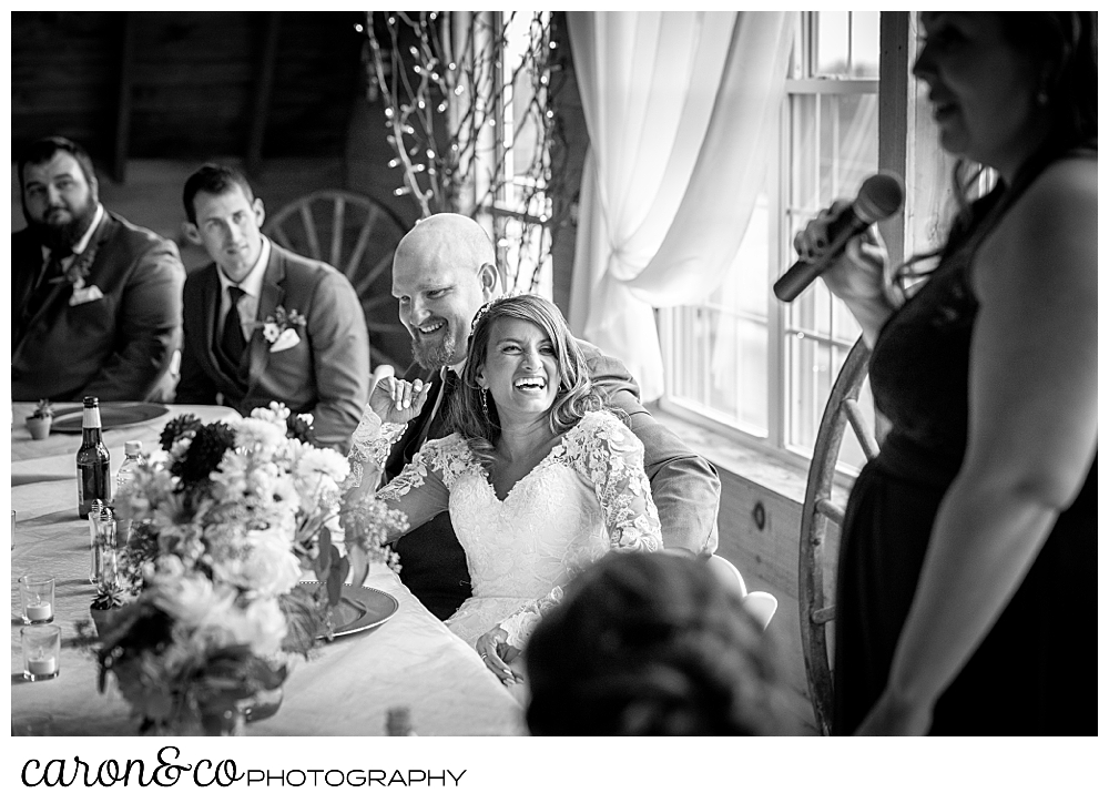 black and white photo of a bride and groom laughing in the background, while the maid of honor holds a microphone during her toast