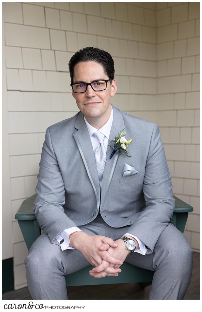 groom portrait of a man in a grey suit, siting in a chair, clasping his hands in front