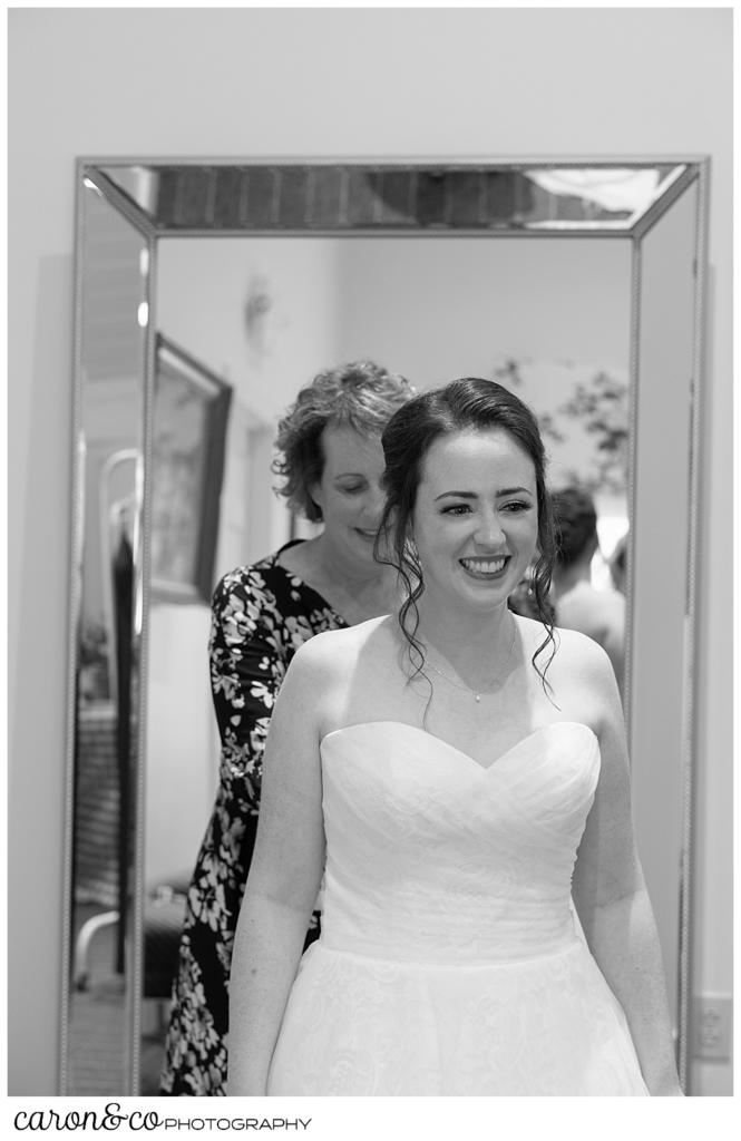 black and white photo of a bride standing in front of a mirror, and her mother fastening her dress behind her