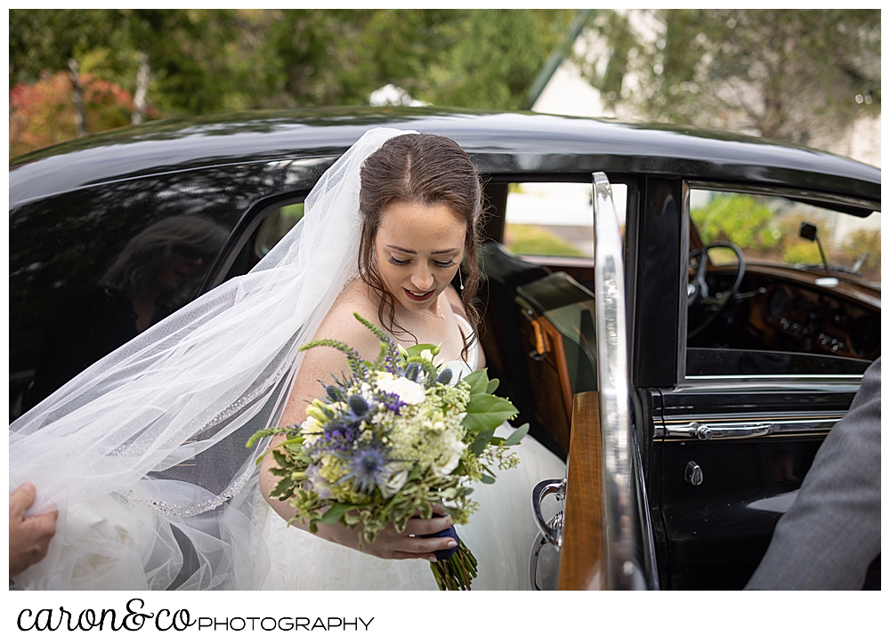a bride wearing a white dress and veil, with a white, yellow, green, and purple bouquet, gets into a vintage Bentley