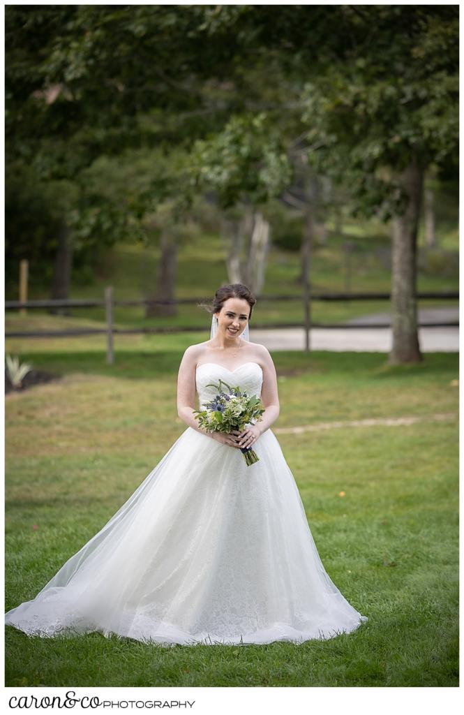 a bride in a full, white strapless dress, holding a white, yellow, green, and purple bouquet, waits for her groom during their wedding day first look