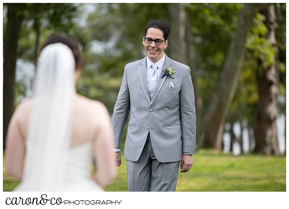 a smiling groom in a gray suit, walks towards his bride during their wedding day first look