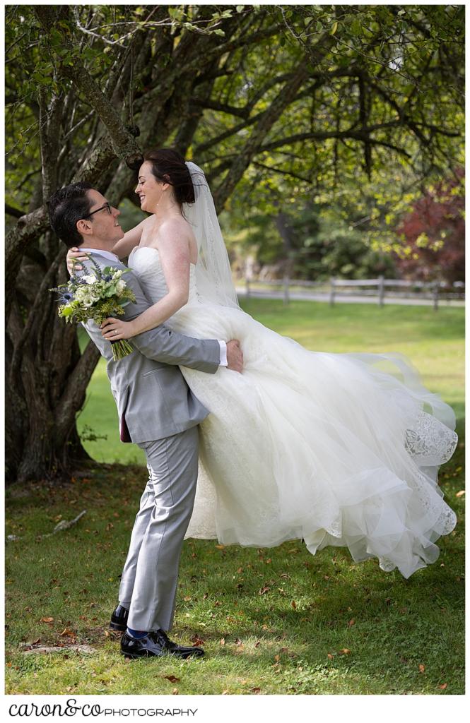 a groom in gray, picks up his bride, wearing white