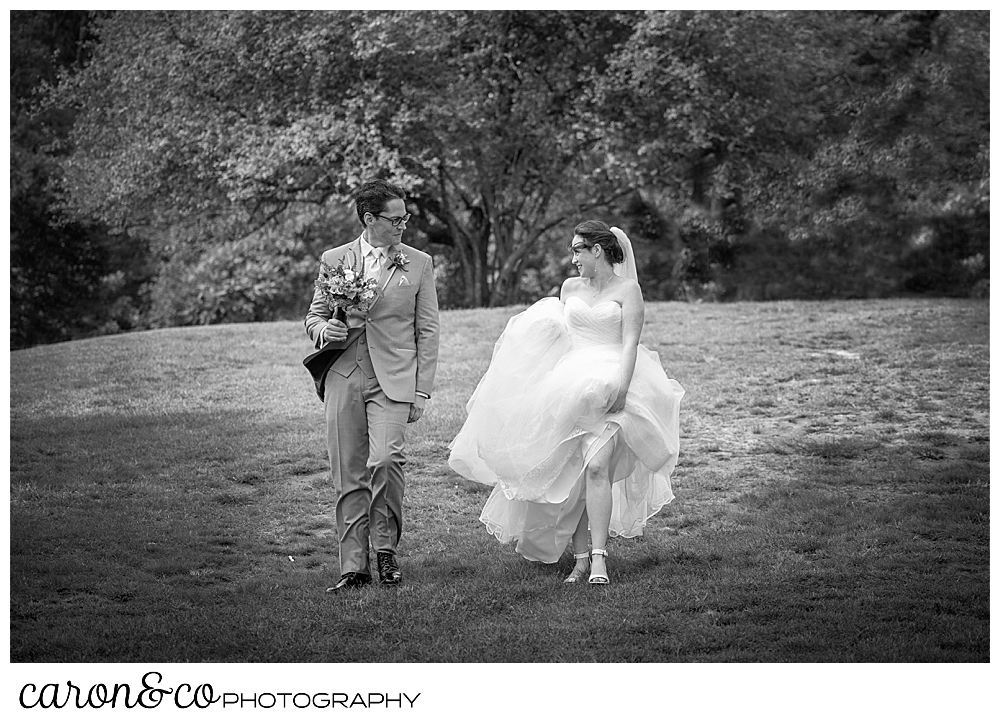 black and white photo of a bride, holding up her dress, walking beside her groom