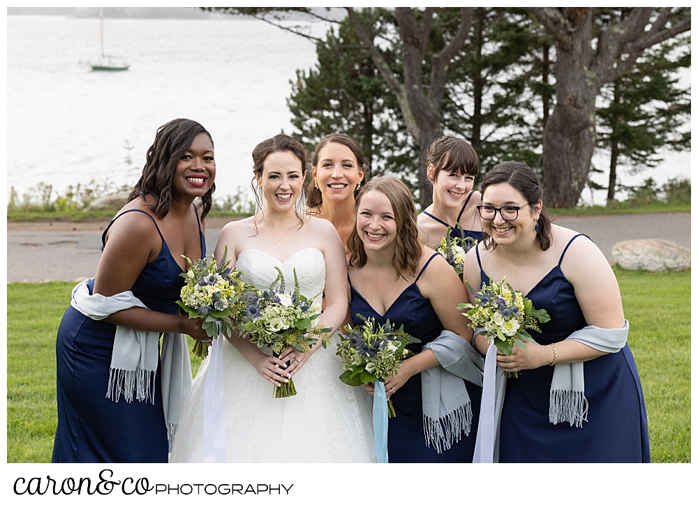 a bride in white, and five bridesmaids in blue, huddle together for a fun photo
