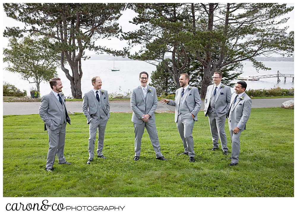 a groom and five groomsmen wearing light gray suits, stand together on the front lawn of the Spruce Point Inn, Boothbay Harbor, Maine