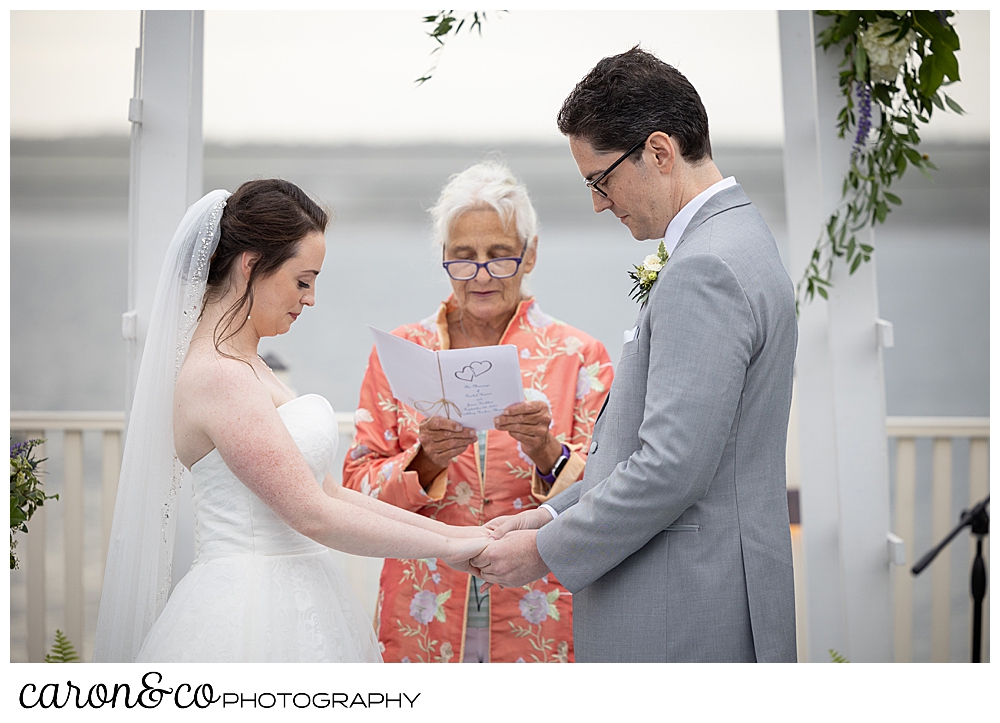 a bride and groom bow their heads before their officiant, Sally Bullard, at their Spruce Point Inn Maine wedding ceremony