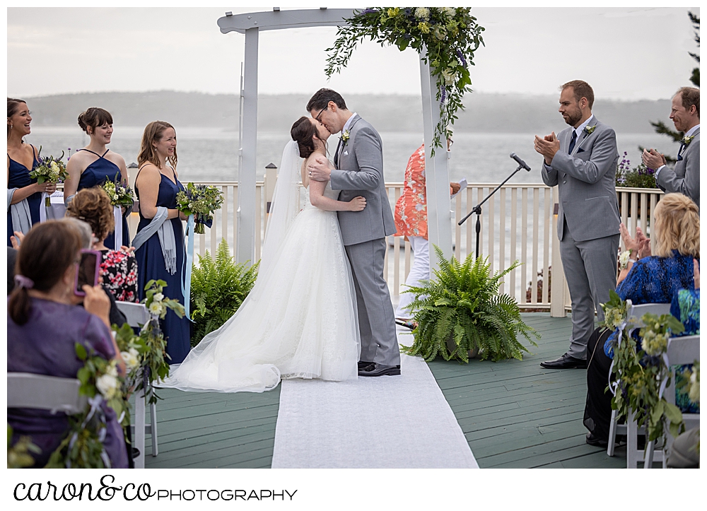 a bride and groom enjoy their first kiss on the deck of an outdoor Spruce Point Inn Maine wedding ceremony