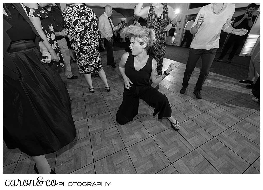 black and white photo of a woman wearing a dark jumpsuit, playing air guitar while kneeling on the dance floor at a Spruce Point Inn Maine wedding, Boothbay Harbor, Maine