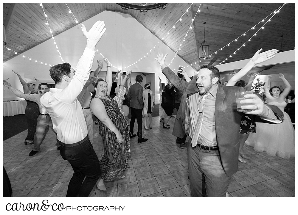 black and white photo of wedding guests dancing, their arms in the air, at a wedding reception