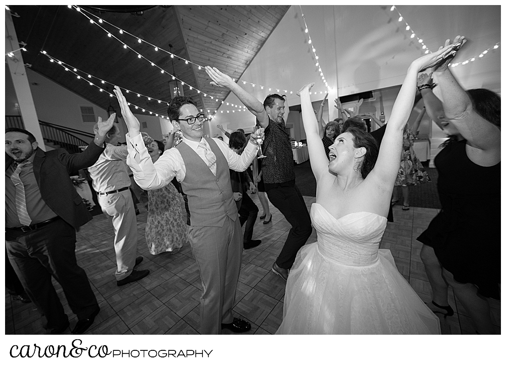 black and white photo of a bride and groom dancing with their arms raised during their Spruce Point Inn Maine wedding reception