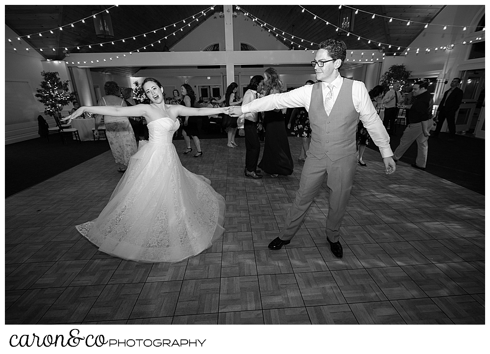 black and white photo of a bride and groom dancing, they're holding hands, their arms out straight, and the bride's dress is swirling, during their Spruce Point Inn Maine wedding reception