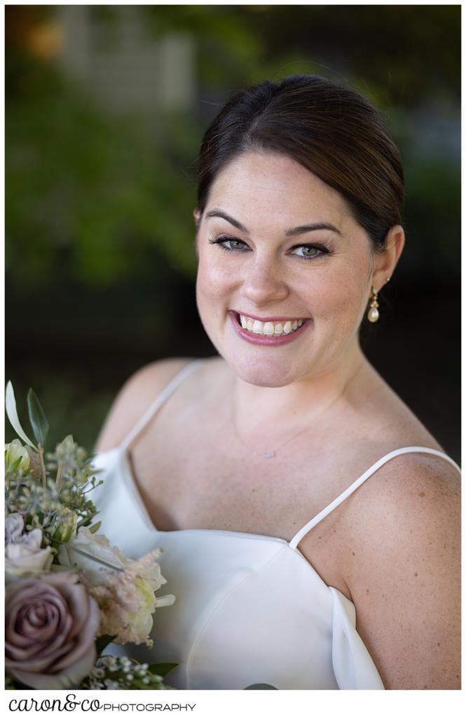 a beautiful bridal portrait of a smiling bride, wearing a white dress with spaghetti straps, holding a bouquet of pink, white and green