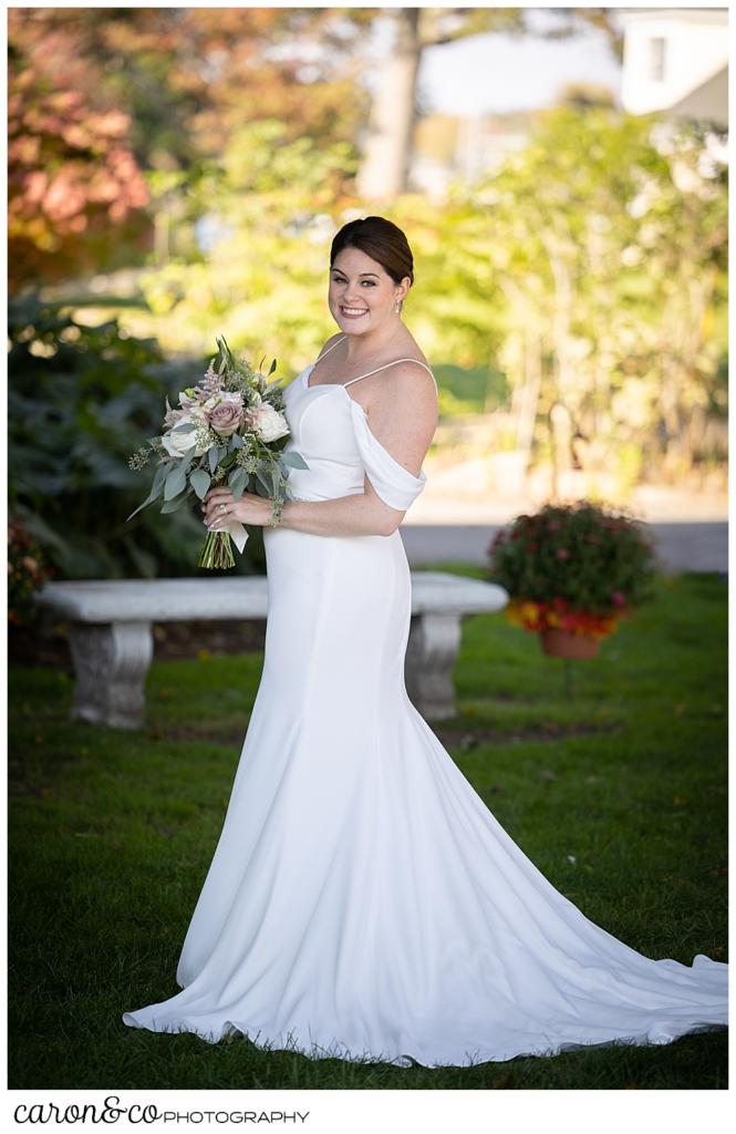 a full length bridal portrait of a bride wearing a whit dress with spaghetti straps, holding a bouquet of cream, pink, and green