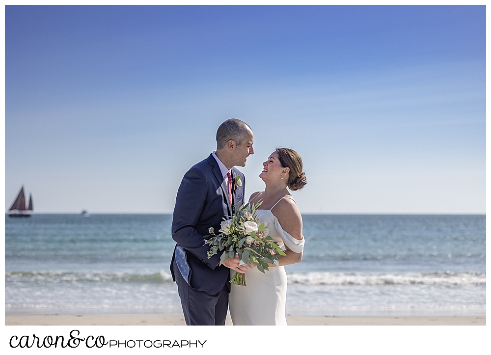 a bride and groom stand together, smiling at each other, on Gooch's Beach, Kennebunk, maine
