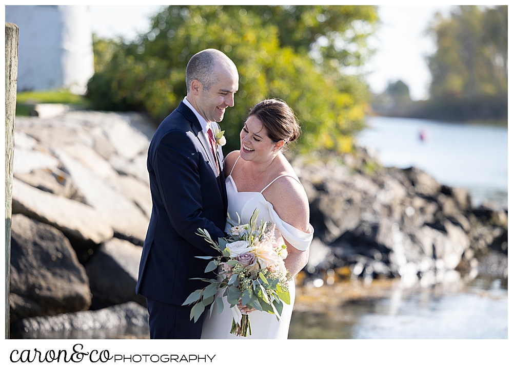 a bride and groom stand on the dock at The Nonantum Resort, Kennebunkport, Maine. They're holding each other and laughing