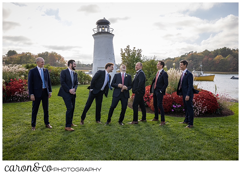 a groom and his groomsmen wearing navy suits, stand together and laugh on the lawn at The Nonantum Resort, Kennebunkport, Maine