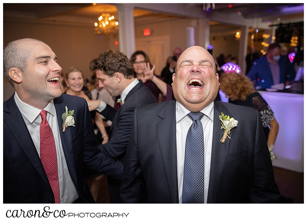 a father of the bride is laughing, his head thrown back, eyes closed, while his new son-in-law looks on and laughs
