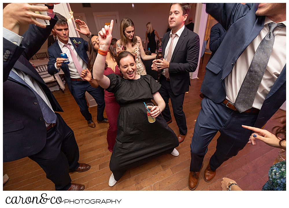 a woman wearing a black dress, holding a drink in one hand, dances at a Nonantum Resort Kennebunkport Maine wedding reception
